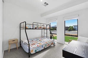 A bunk bed room with a small wooden side table, a large window with a view of the outside, and a carpeted floor. - Stillwater - holiday home with a private jetty (Wellington East)