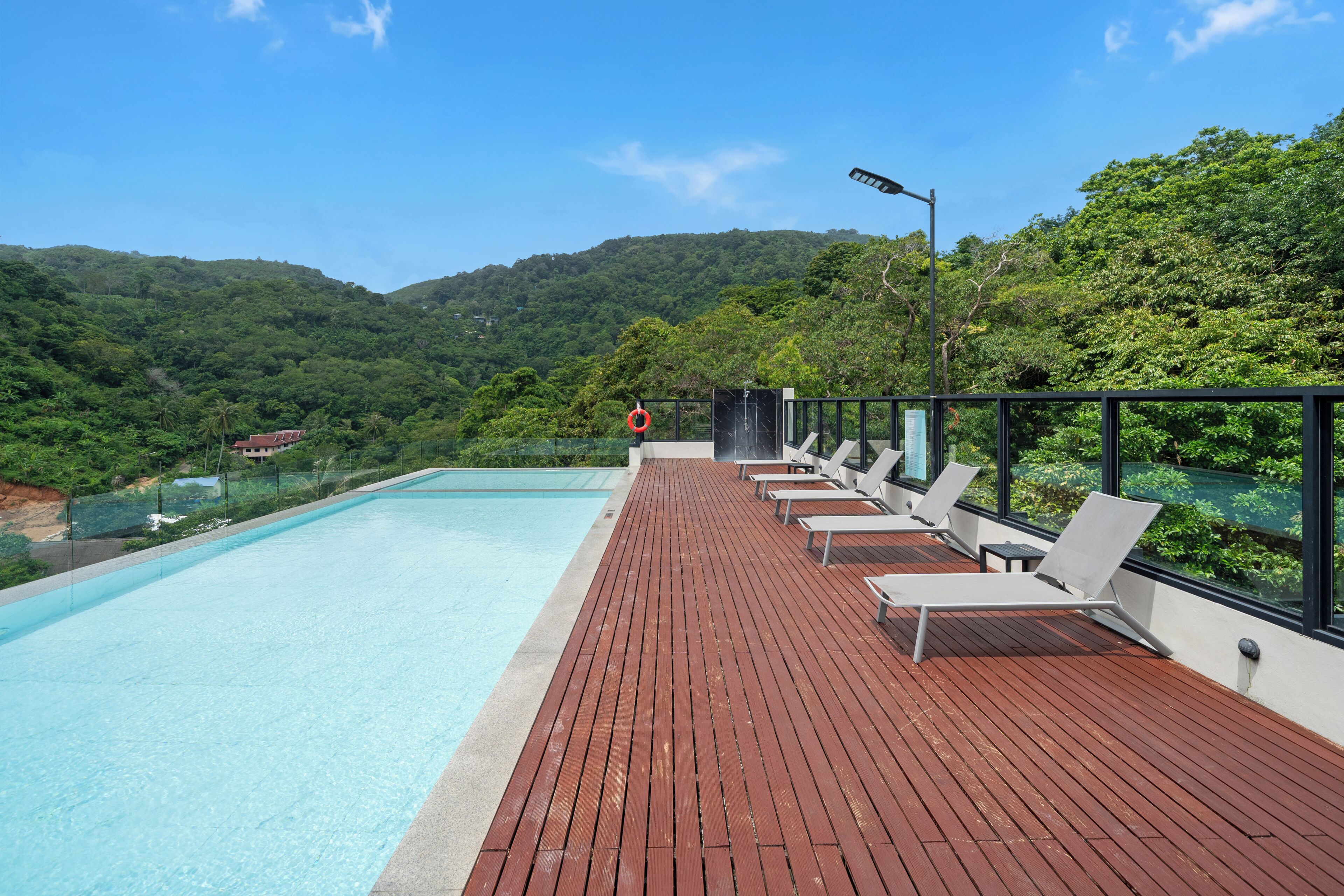 Una piscina con un pontile in legno e poltronne da relax, circondata da una vegetazione lussureggiante e dolci colline.