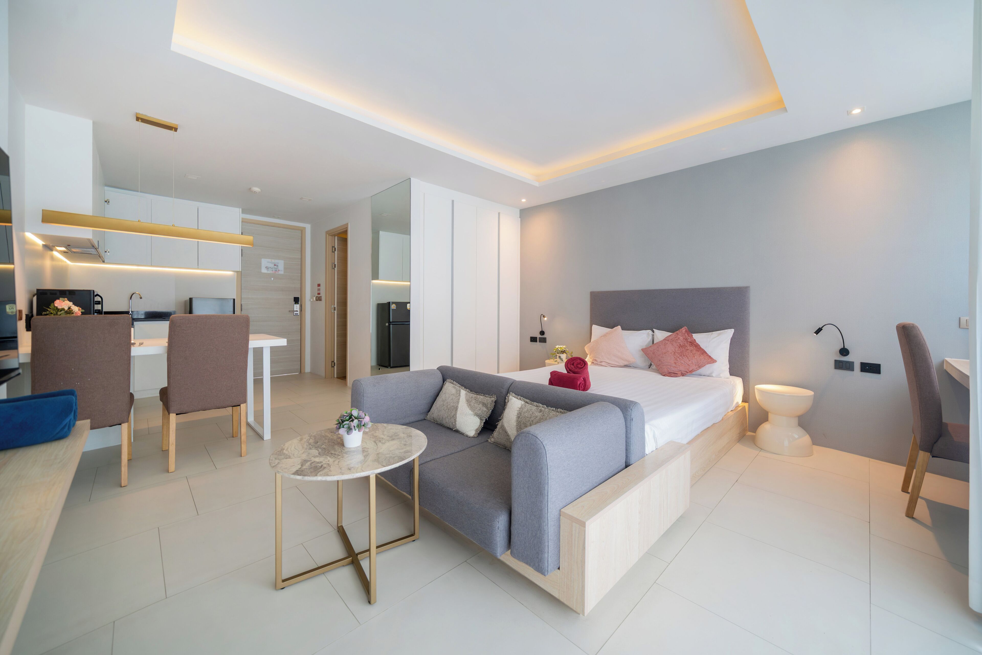 Habitación de hotel moderna con cama, sofá, mesa de comedor y kitchenette.