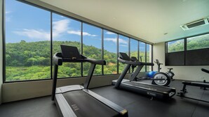 Uma academia com esteiras e equipamentos de ginástica, janelas amplas com vista para uma paisagem arborizada.