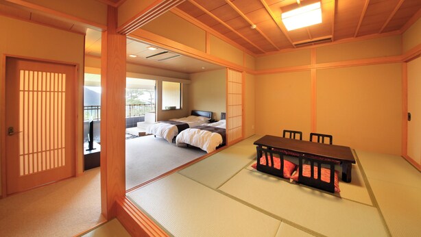 Une pièce de style japonais traditionnel, avec un sol recouvert de tatamis, une table basse entourée de chaises et un lit équipé d’un futon.