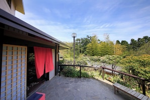 A stone-paved balcony with a wooden railing overlooking a garden.