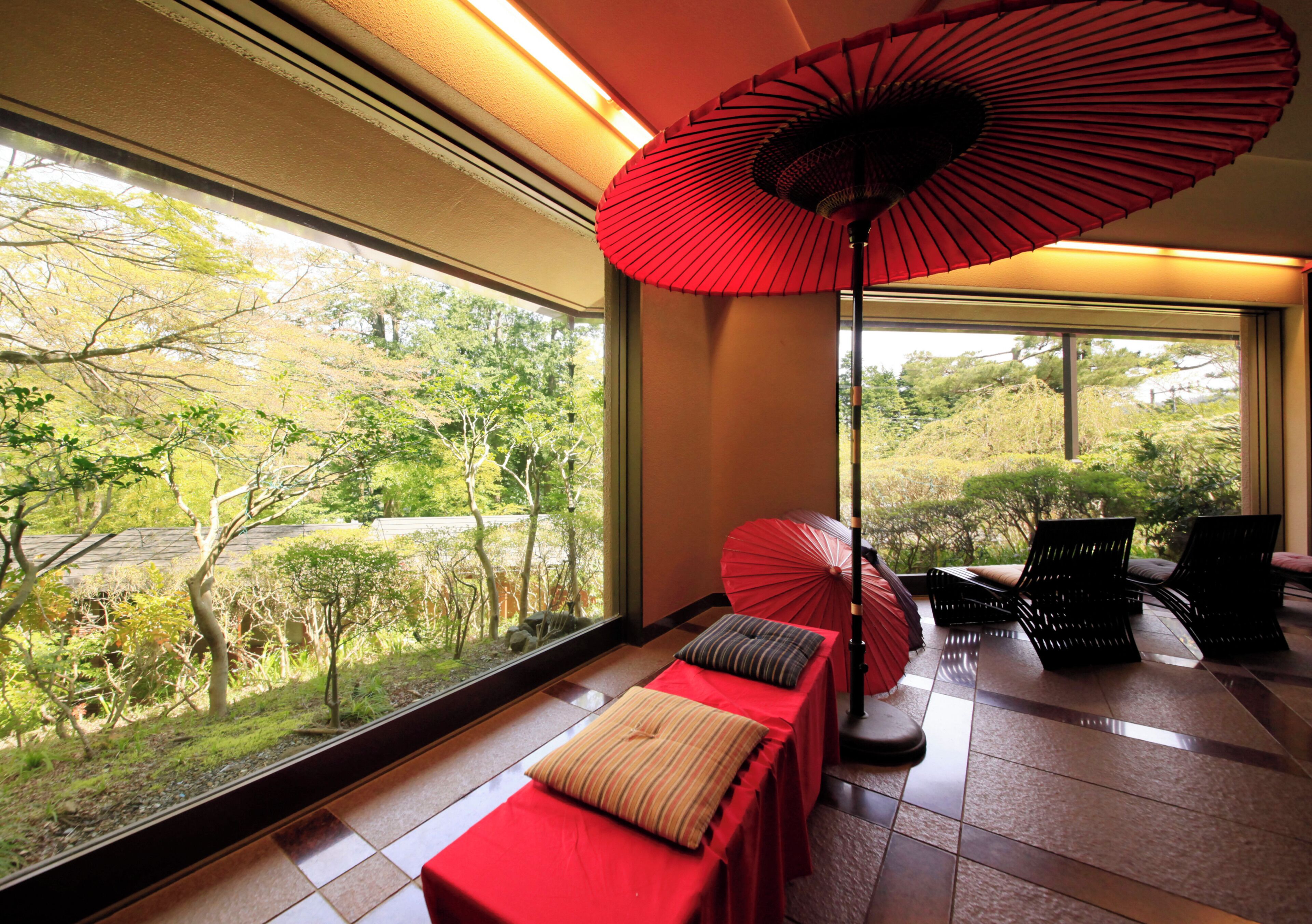 Una habitación con un ventanal grande, un paraguas rojo y un banco con almohadones.