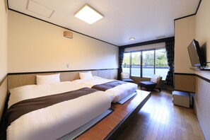 Une chambre d’hôtel avec deux lits, un petit coin salon, une télévision et une fenêtre donnant sur l’extérieur.