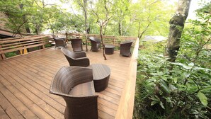 Une terrasse en bois, meublée de meubles en osier, entourée d’arbres.