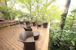 Una terraza de madera con mobiliario de mimbre, rodeada de árboles.