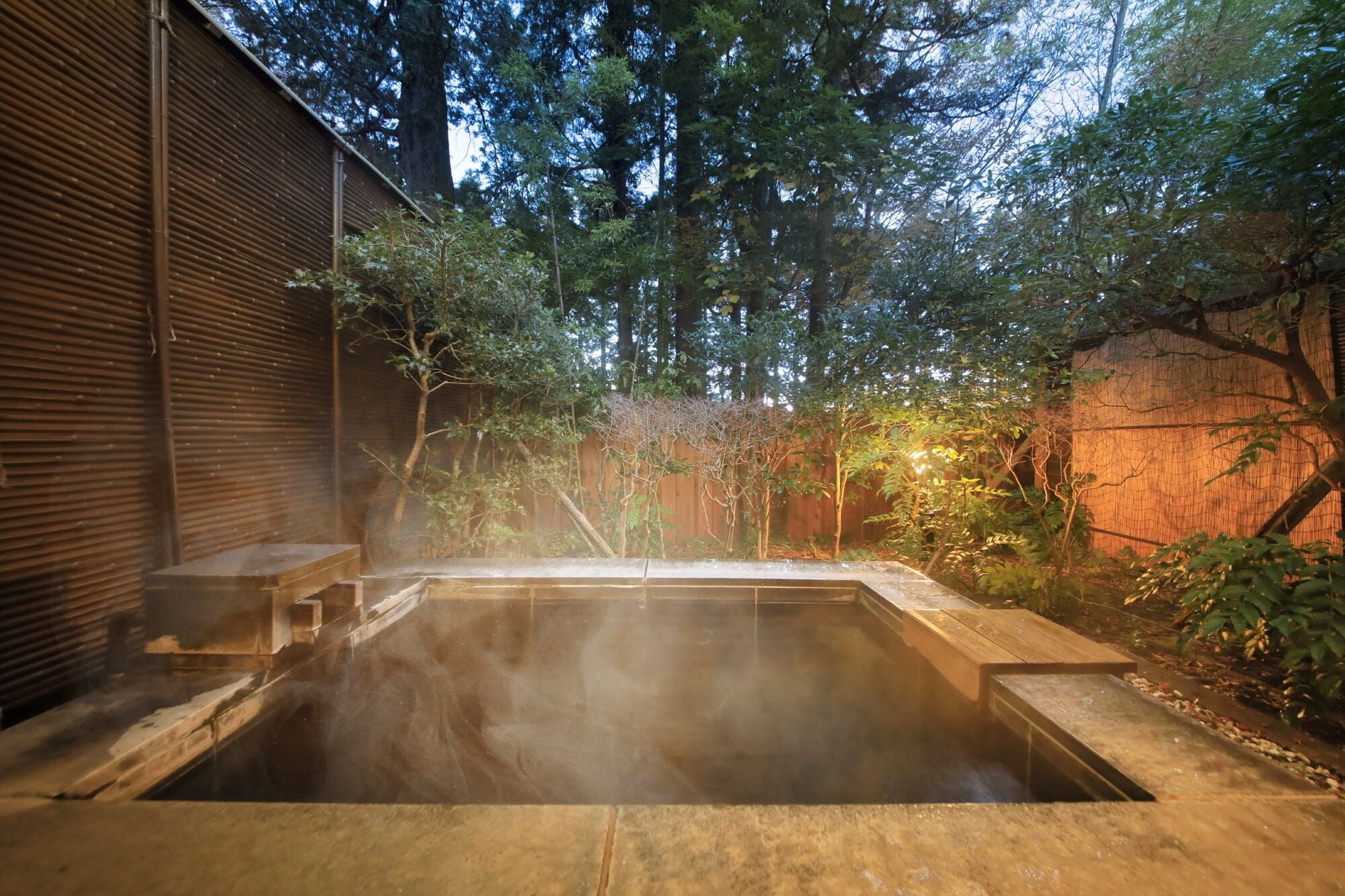 Un jacuzzi rodeado de una valla de madera y árboles, con una vista despejada del cielo.