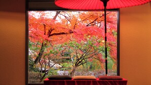 Une pièce dotée d’une grande fenêtre donnant sur un jardin aux couleurs automnales.