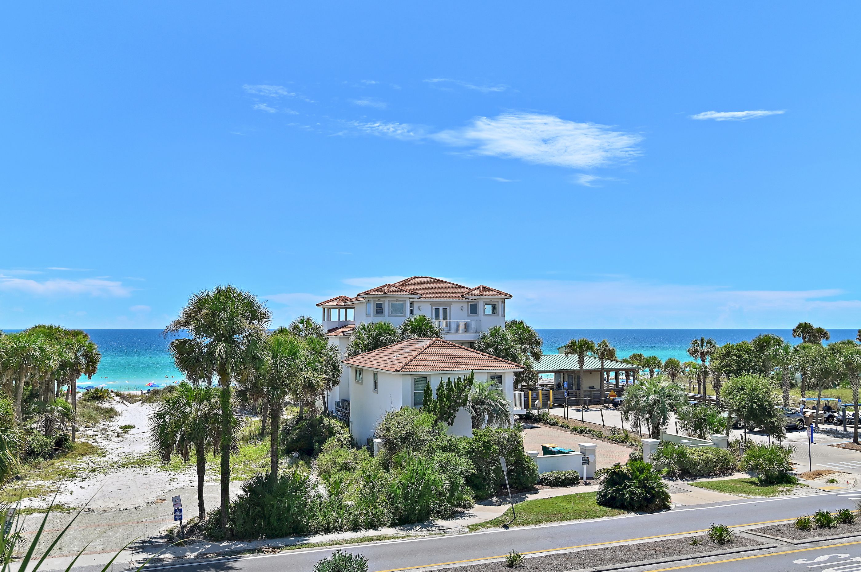 A beachfront property with a two-story building, a paved road, and a beach in the background.