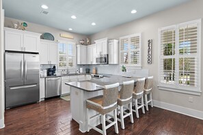 A modern kitchen with white cabinetry, stainless steel appliances, a central island with bar stools, and a sign reading 'SEAFOOD'. - Steps2 Beach/Gulf Views/Heated Pool&Spa/Golf Cart (Destin)