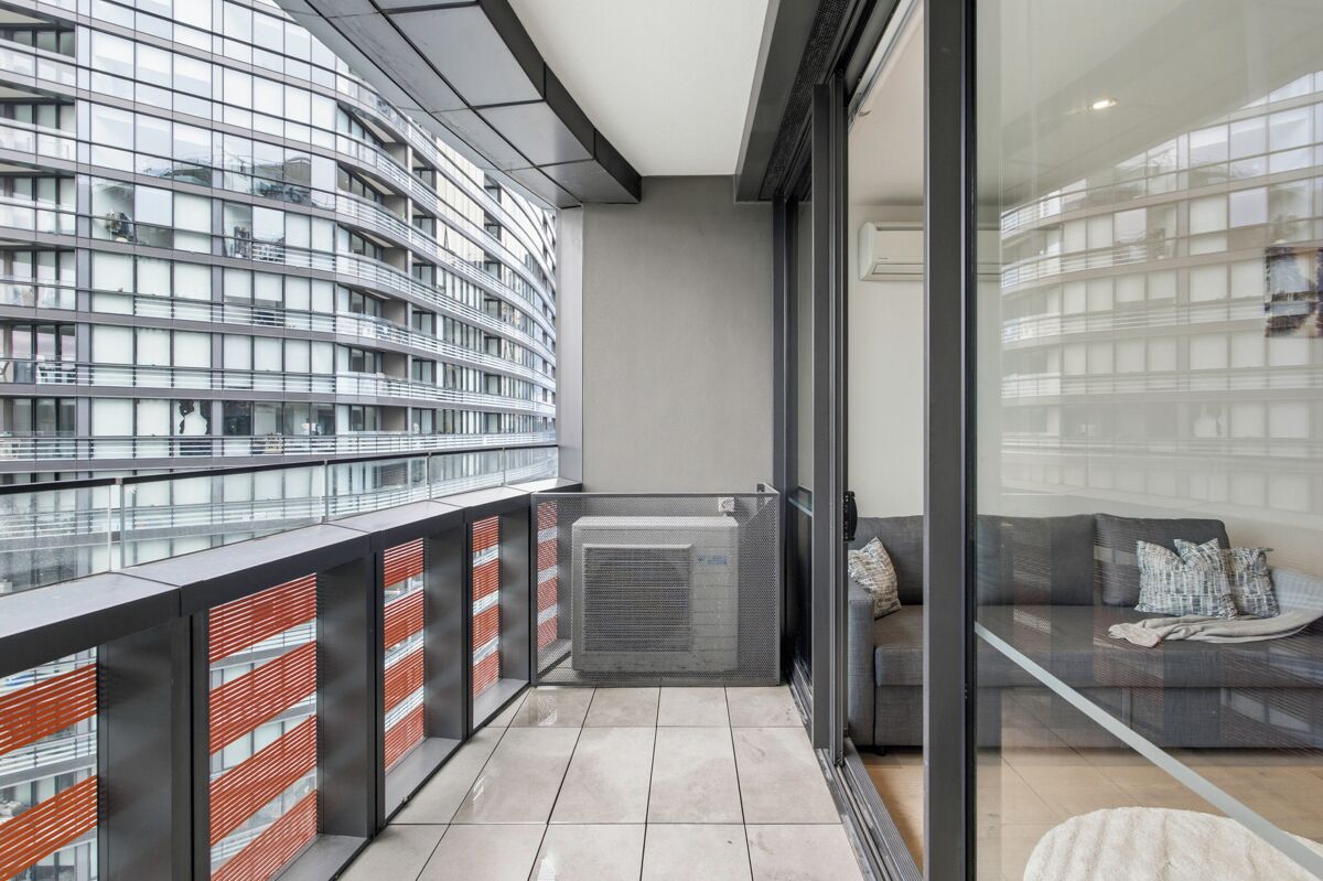 Ein moderner Balkon mit Glastrennwand, einer fest installierten Klimaanlage und Blick auf ein Hochhaus.