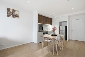 A modern kitchen with white cabinets, a wooden dining table, and a vase with flowers. - Melbourne Executive Suites | Collins Street | Docklands | Free Parking Onsite (Docklands)