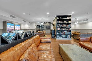 A modern lounge area with leather seating, a large bookshelf, and a city view through large windows. - High-Rise 1-Bed Apartment Near Southern Cross (Melbourne)