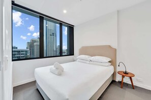 Ein Hotelzimmer mit großem Fenster, einem Bett mit weißer Bettwäsche, einem runden Holzhochentisch und einem modernen Kopfteil.