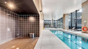 En moderne indendørs swimmingpool med krystalklart vand, flisebeklædte vægge og et solbelyst loft.