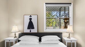 Ein Schlafzimmer mit einem Bett, zwei Nachttischen, einem Fenster mit Moskitonetz und einem gerahmten Bild an der Wand.
