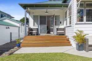 Ein zweigeschossiges Haus mit einer Veranda, einer Holztreppe, die zum Eingang führt, und einem kleinen Garten mit Blumentöpfen.