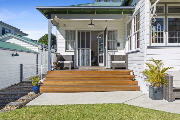 A two-story house with a porch, a set of wooden steps leading to the entrance, and a small garden area with potted plants.