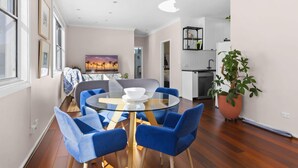 Ein modernes Wohnzimmer mit einem runden Glastisch, blauen Stühlen, einem Sonnenuntergangsgemälde und Blick in den Küchenbereich.