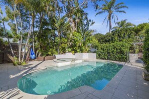 A swimming pool with a sunken seating area, surrounded by lush greenery and tall palm trees.