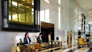 Un hall d’hôtel avec un comptoir d’accueil, des luminaires modernes et une grande fenêtre.