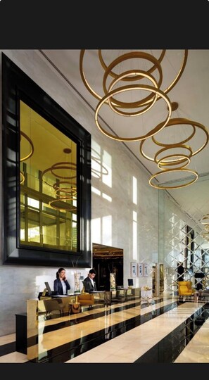 Un hall d’hôtel avec un comptoir d’accueil, des luminaires modernes et une grande fenêtre.