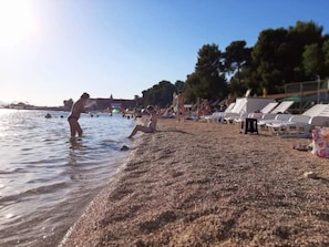 En strand med folk som badar och solar, och en rad strandstolar.
