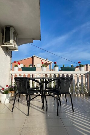 Ein Balkon mit Tisch und Stühlen, Blumentöpfen und einem Gebäude im Hintergrund.