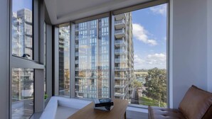 A modern living room with a sofa, a coffee table, and a view of high-rise buildings through large windows. - Skyline-View 2-Bed Apartment Near Flemington (Flemington)