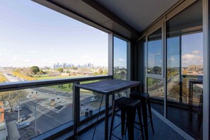 A balcony with a view of a city skyline, a table, and two bar stools. - Skyline-View 2-Bed Apartment Near Flemington (Flemington)