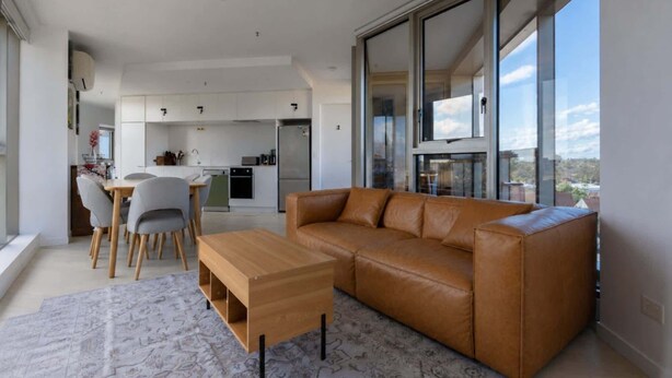 A modern living room with a leather sofa, a wooden coffee table, and a patterned rug. - Skyline-View 2-Bed Apartment Near Flemington (Flemington)