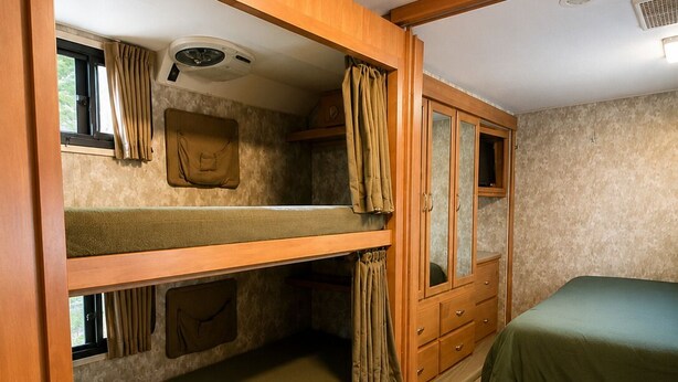 Una camera da letto compatta per camper con cuccette a castello, un armadietto e un piccolo oblò.