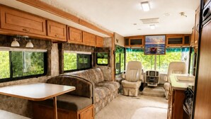 Interno di un camper con zona pranzo, posti a sedere e angolo cottura.
