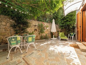 An outdoor patio with stone walls, a table with chairs, and a covered area with an umbrella. - Apartment Lu by Interhome (Krk/Milohnići)