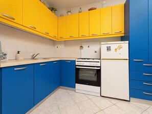 A kitchen with yellow upper cabinets, a white refrigerator, and a stove. - Apartment Lu by Interhome (Krk/Milohnići)