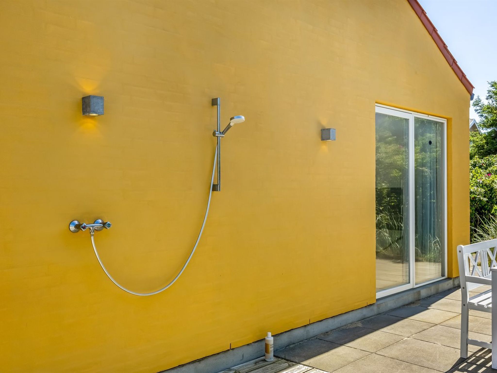 Un bâtiment jaune doté d’une porte coulissante en verre, d’une douche et d’un petit espace extérieur aménagé pour s’asseoir.