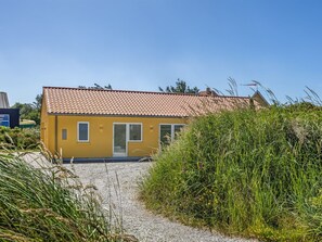 Ein gelbes Gebäude mit einem Ziegeldach und einer Schotterauffahrt, die zu einer Glastür führt.