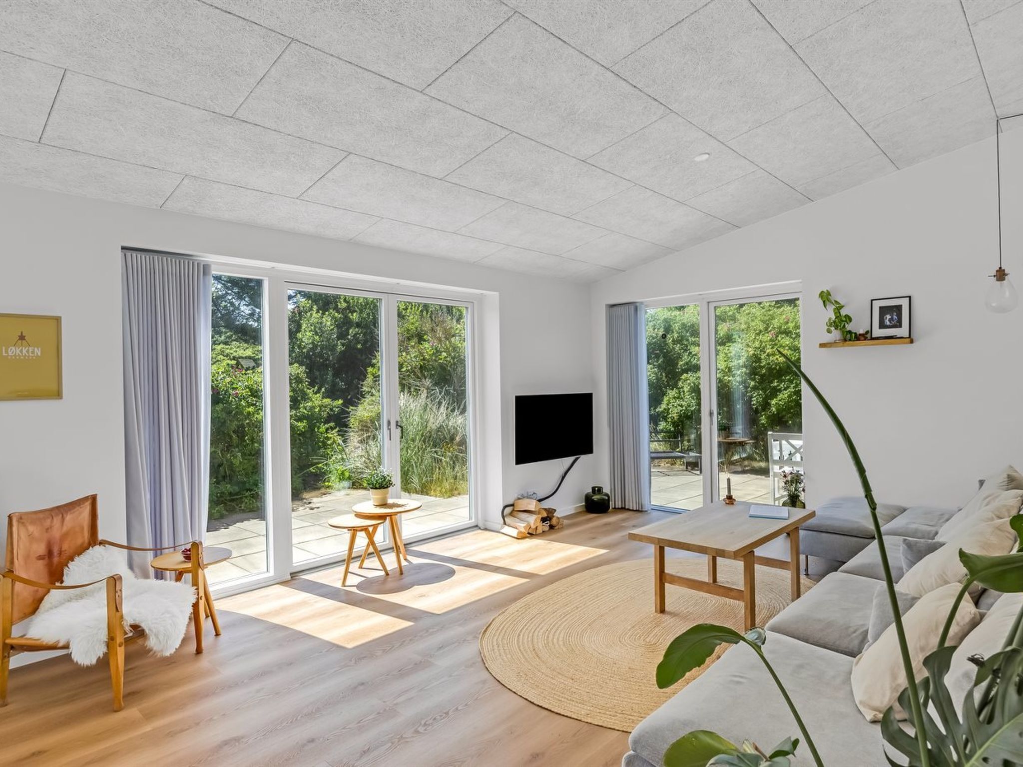 Un salon moderne comprenant un canapé, une table basse, un téléviseur et une grande fenêtre donnant sur un paysage verdoyant.