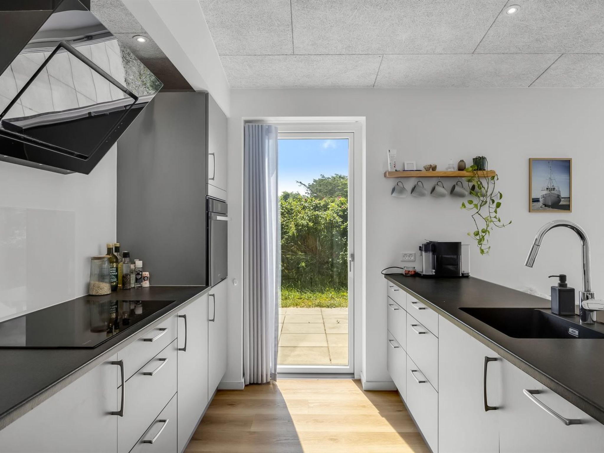 Une cuisine moderne avec un plan de travail noir, des armoires blanches et une vue sur l’extérieur.