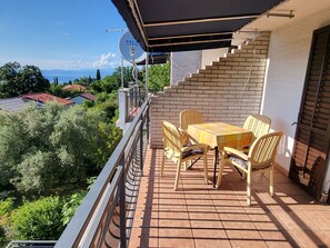 Een balkon met een tafel en stoelen, een schotelantenne en uitzicht op zee en huizen.