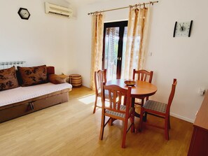 Ein Zimmer mit einer Couch, einem Holzespeisetisch, Stühlen und einem Fenster mit Vorhängen.