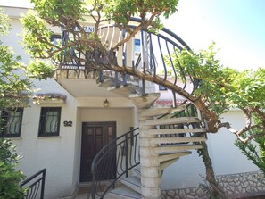 Ein Gebäude mit einer Wendeltreppe, einer Tür mit der Nummer 92 und einem Baum mit grünen Blättern.