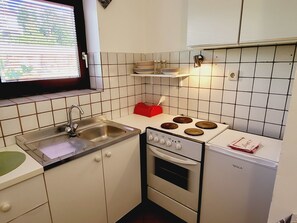 Eine kompakte Küche mit Spüle, Herd, Backofen und einem Fenster mit Jalousien.
