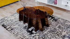 Een ronde houten salontafel met een glazen blad, rustend op vier poten, geplaatst op een vloerkleed met dessin.
