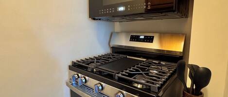 A kitchen with a black stove, wooden cabinets, and a stainless steel range hood.