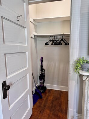 A hallway with a white door, a vacuum cleaner, a hanging clothes rack, and a potted plant. - Park Views-3, Cozy, Quiet, Clean, Central Location (Bloomington)