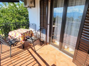 Eine Terrasse mit Tisch und Stühlen, eine Schiebeglastür und Blick ins Grüne.