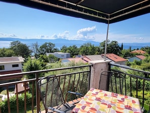 Un balcon donnant sur un lac et des montagnes, avec des rampes en métal et une table recouverte d’une nappe colorée.