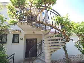 Un bâtiment doté d’un escalier en colimaçon, une porte portant le numéro 92 et un arbre aux feuilles vertes.
