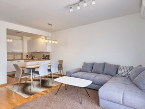 A modern living room with a grey sofa, a white coffee table, and a dining area with chairs and a kitchen in the background. - Mara spacious apartment with pool by Interhome (Medulin/Ližnjan)